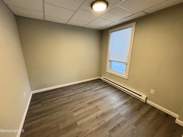 empty room featuring a drop ceiling, a baseboard radiator, and wood-type flooring