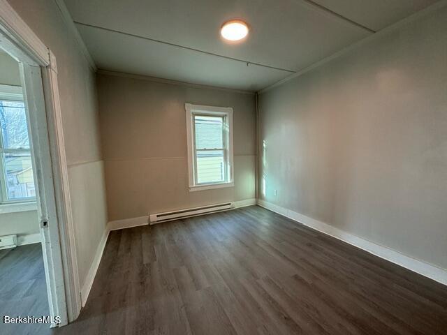 spare room with a baseboard radiator, ornamental molding, and dark wood-type flooring