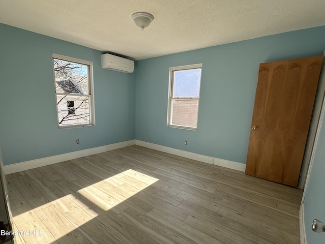 empty room with a wall mounted AC, light hardwood / wood-style floors, and a wealth of natural light