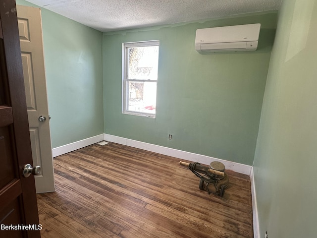 spare room with dark hardwood / wood-style floors, a wall unit AC, and a textured ceiling