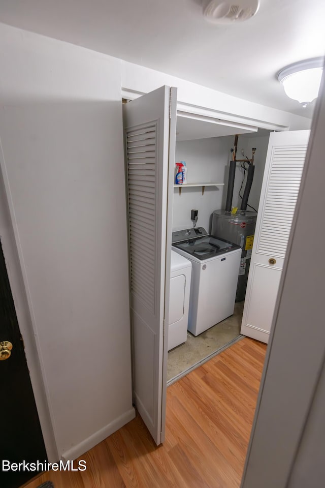 clothes washing area featuring laundry area, washing machine and dryer, water heater, and light wood finished floors