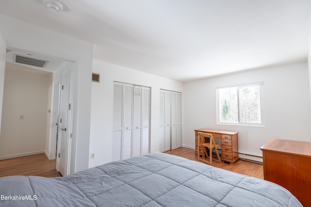 bedroom with multiple closets, a baseboard heating unit, visible vents, and wood finished floors