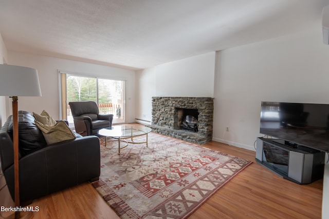 living area featuring a stone fireplace, a baseboard radiator, wood finished floors, and baseboards