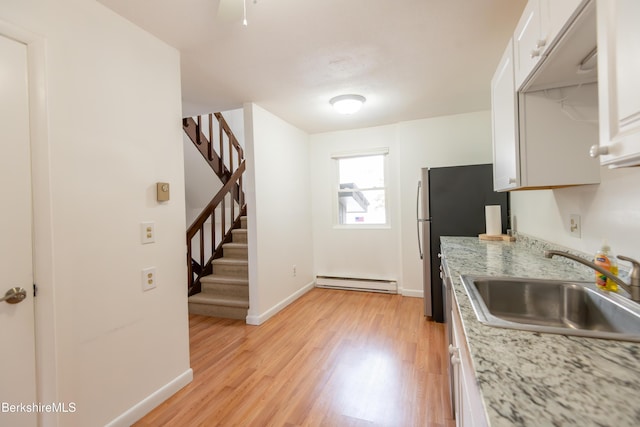 kitchen with a sink, white cabinetry, baseboards, baseboard heating, and light wood finished floors