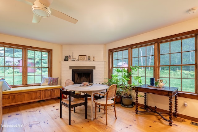 dining room with ceiling fan, a brick fireplace, light wood finished floors, and plenty of natural light