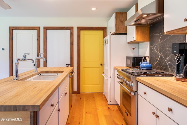 kitchen with butcher block counters, wall chimney range hood, stainless steel appliances, and a sink