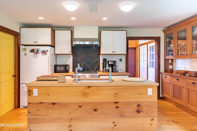 kitchen with tasteful backsplash, light wood-type flooring, freestanding refrigerator, wall chimney range hood, and black microwave