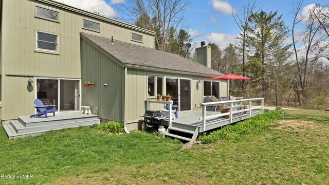 rear view of property featuring a shingled roof, a wooden deck, a yard, and a chimney