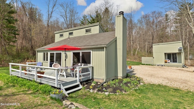 back of property featuring an outbuilding, a chimney, a shingled roof, and a wooden deck