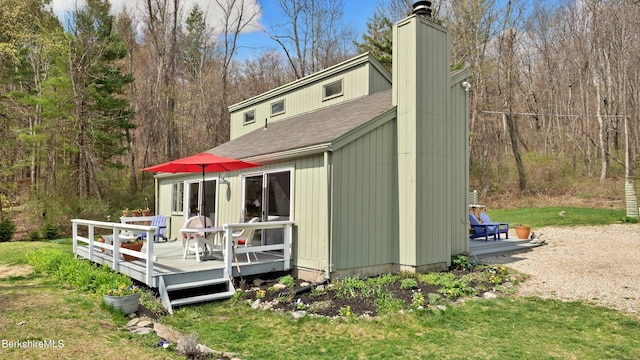 rear view of house with a deck, a shingled roof, a forest view, and a chimney