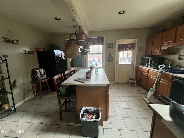 kitchen with sink, light tile patterned floors, a breakfast bar, a kitchen island, and black appliances