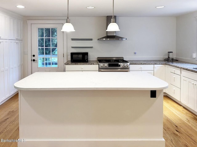 kitchen featuring gas range, wall chimney exhaust hood, black microwave, white cabinets, and light wood-type flooring