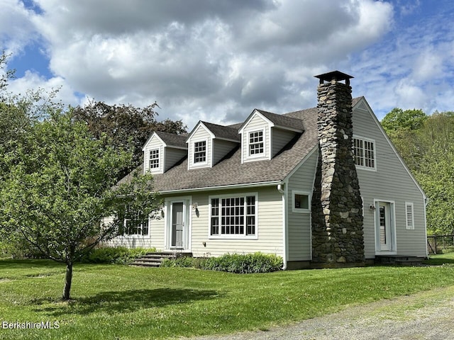 new england style home with a shingled roof, a front yard, and a chimney