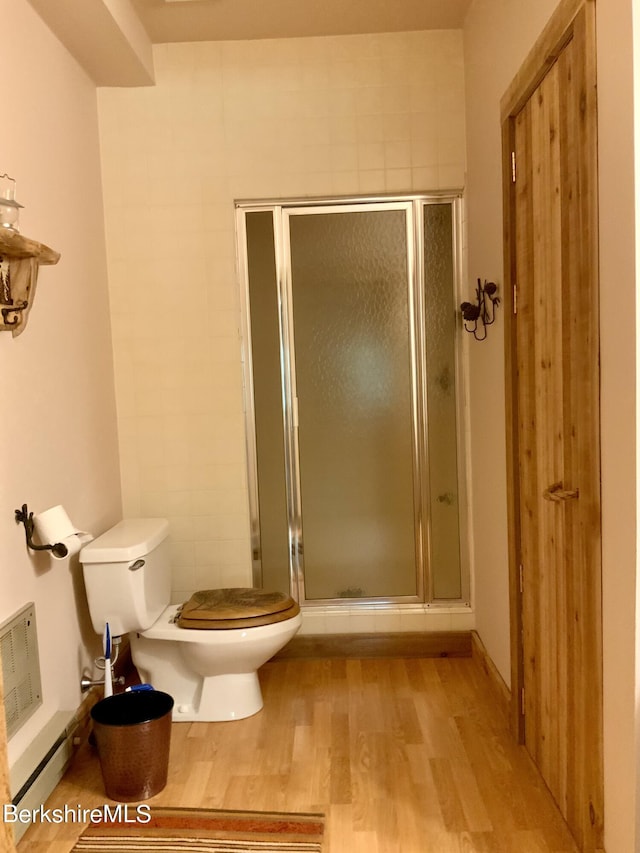 bathroom with baseboard heating, a shower stall, toilet, and wood finished floors