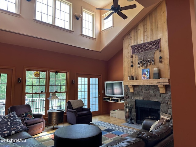 living room with a stone fireplace, wood finished floors, a towering ceiling, and ceiling fan