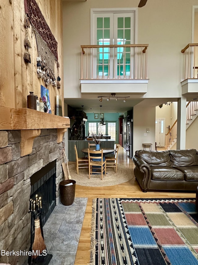 living room featuring a stone fireplace, a high ceiling, stairs, and wood finished floors