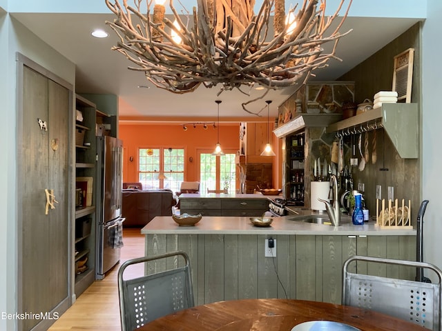 kitchen featuring open shelves, light wood-style flooring, freestanding refrigerator, a sink, and decorative light fixtures