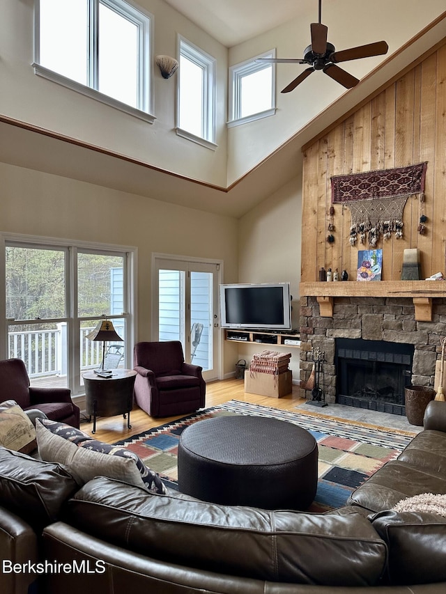 living room with a towering ceiling, a fireplace, a ceiling fan, and wood finished floors