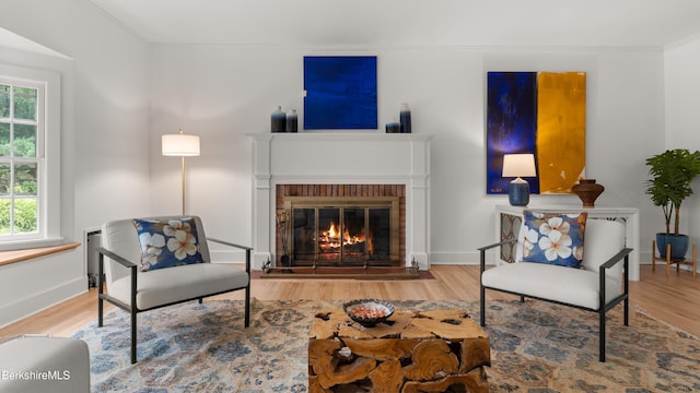 living room with healthy amount of natural light, wood finished floors, a brick fireplace, ornamental molding, and baseboards