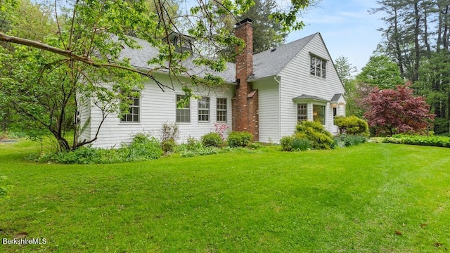 view of side of home with a yard, a chimney, and a shingled roof