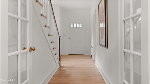 hallway with light wood-type flooring, baseboards, and stairway