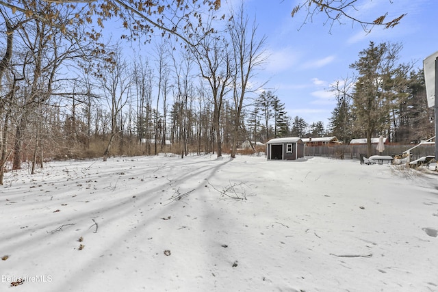 yard covered in snow with an outbuilding, a storage unit, and fence