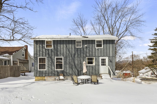 snow covered property with entry steps, fence, and board and batten siding