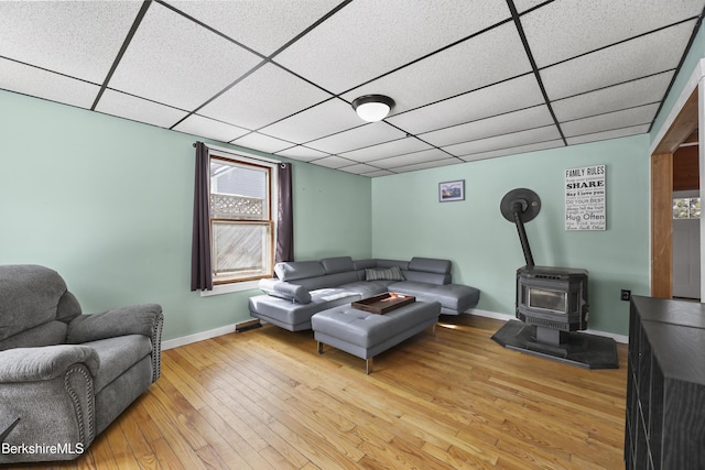 living area with a wood stove, light wood-style floors, baseboards, and a paneled ceiling