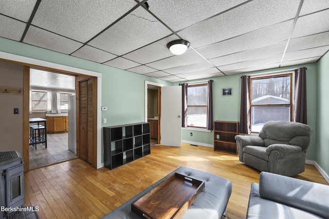 living area featuring a paneled ceiling, light wood-style flooring, and baseboards