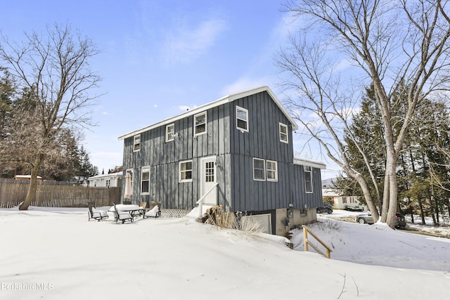 snow covered back of property featuring board and batten siding, fence, and an attached garage