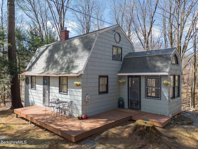 back of property with roof with shingles, a deck, a gambrel roof, and a chimney