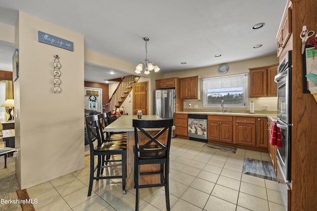 kitchen featuring a kitchen breakfast bar, stainless steel appliances, sink, hanging light fixtures, and light tile patterned flooring