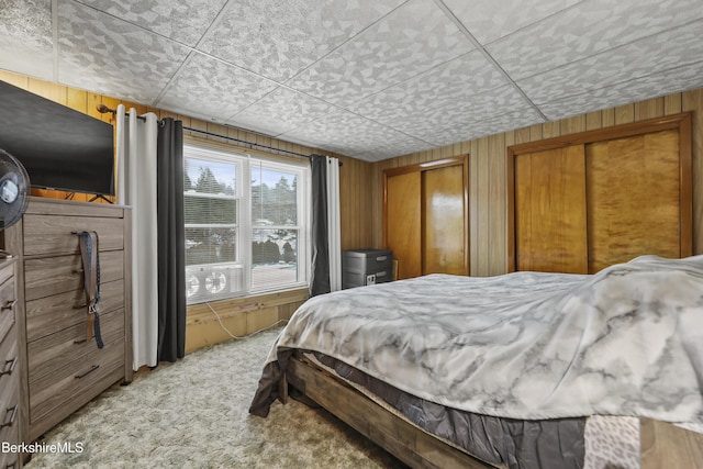 bedroom featuring carpet, multiple closets, and wood walls