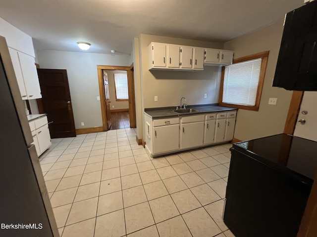 kitchen featuring sink, light tile patterned floors, range with electric stovetop, stainless steel fridge, and white cabinets