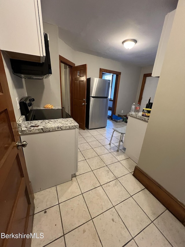 kitchen featuring light tile patterned floors, range with electric stovetop, stainless steel refrigerator, and white cabinets