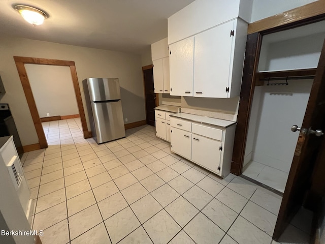 kitchen featuring stainless steel fridge, light tile patterned floors, and white cabinets