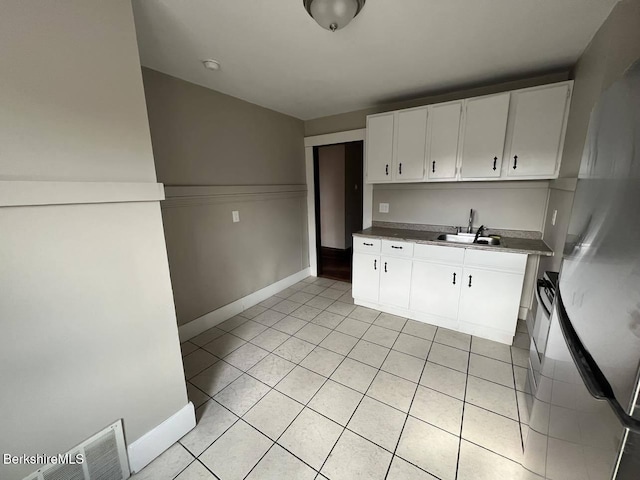 kitchen with sink, light tile patterned floors, white cabinets, and stainless steel refrigerator