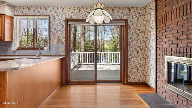 unfurnished dining area with a sink, light wood-style flooring, baseboards, and wallpapered walls