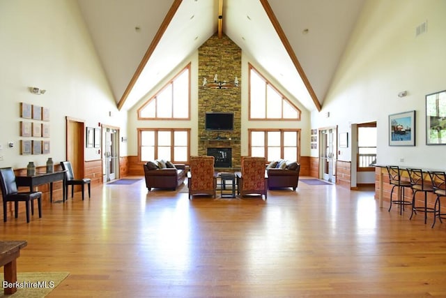 living area with high vaulted ceiling, a healthy amount of sunlight, wood finished floors, and visible vents