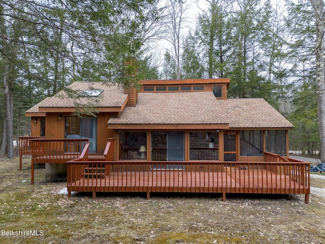 rear view of house featuring a sunroom, a wooden deck, a shingled roof, and a chimney