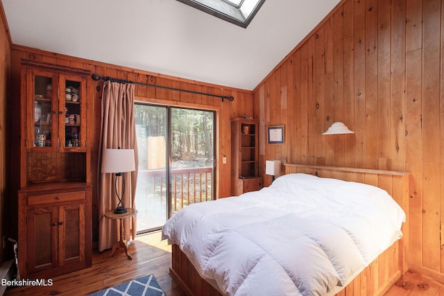 bedroom with wood walls, access to exterior, wood finished floors, and lofted ceiling with skylight