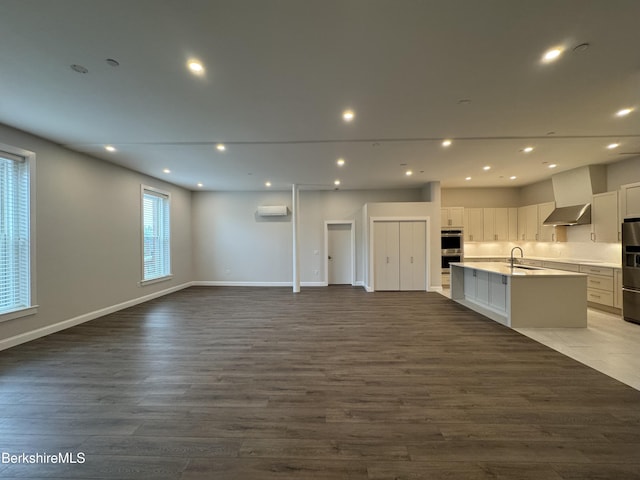 kitchen with an island with sink, white cabinets, stainless steel double oven, open floor plan, and recessed lighting