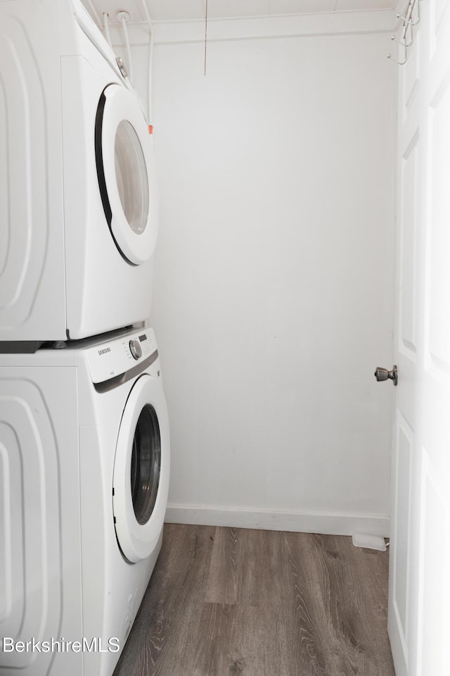 washroom with stacked washer / dryer, laundry area, wood finished floors, and baseboards