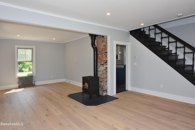 unfurnished living room featuring ornamental molding, a wood stove, light hardwood / wood-style floors, and radiator heating unit