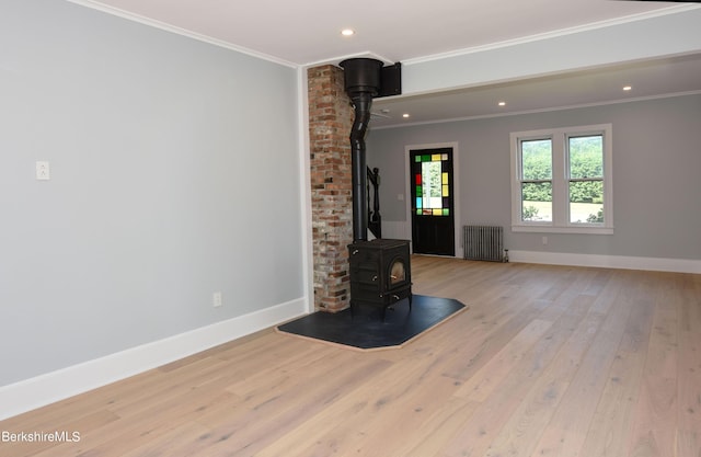 unfurnished living room with ornamental molding, a wood stove, light hardwood / wood-style floors, and radiator heating unit