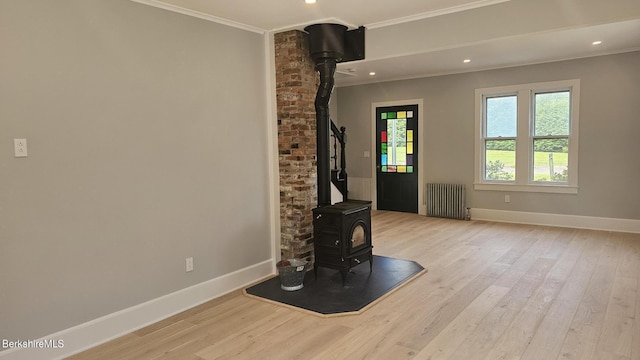 unfurnished living room with light hardwood / wood-style floors, radiator heating unit, crown molding, and a wood stove