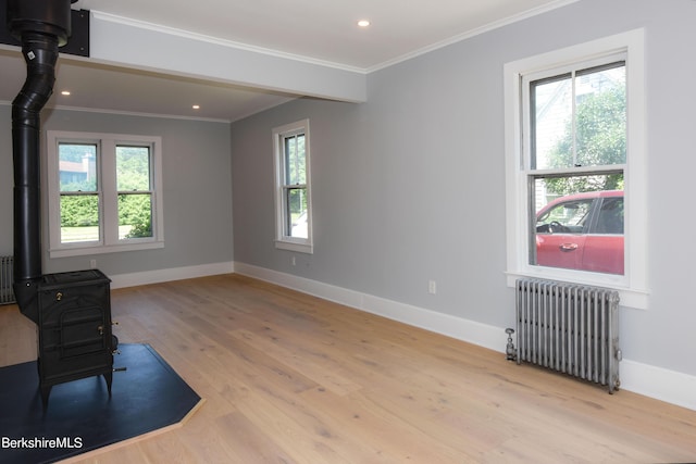 empty room with crown molding, radiator, a wood stove, and light hardwood / wood-style flooring