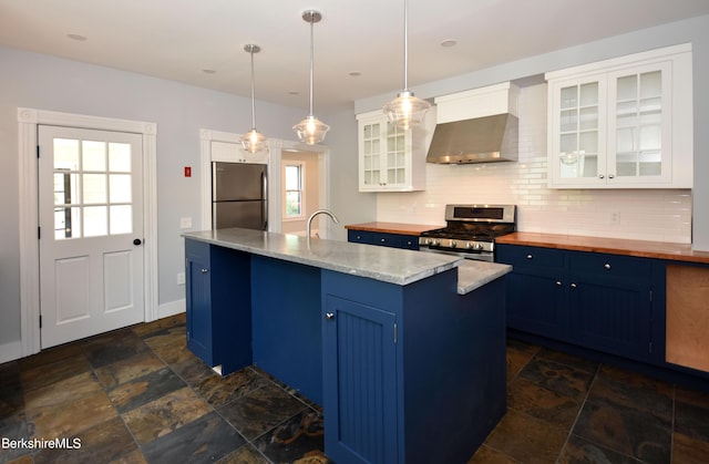 kitchen featuring appliances with stainless steel finishes, hanging light fixtures, wall chimney range hood, and white cabinets