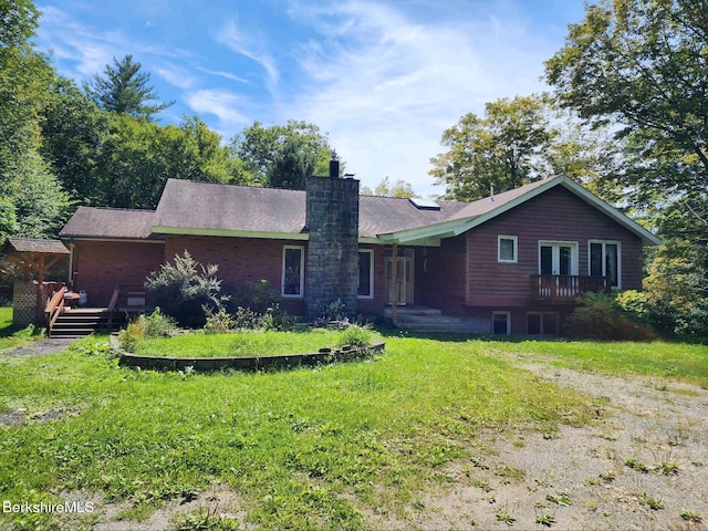 view of front of house featuring a deck, brick siding, a chimney, and a front lawn