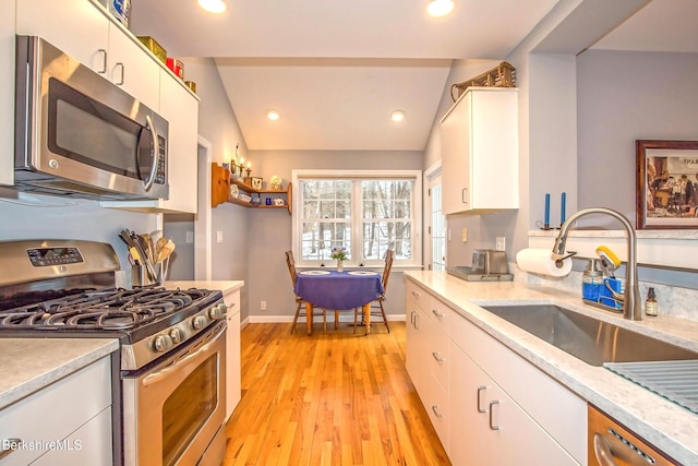 kitchen with lofted ceiling, sink, light hardwood / wood-style flooring, white cabinetry, and stainless steel appliances